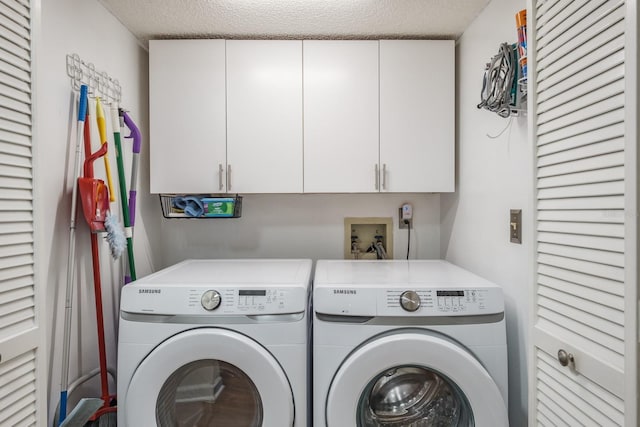 laundry area with washing machine and dryer, a textured ceiling, and cabinets