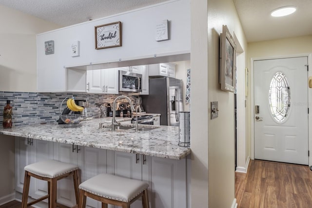 kitchen featuring a kitchen bar, appliances with stainless steel finishes, white cabinets, sink, and light stone counters