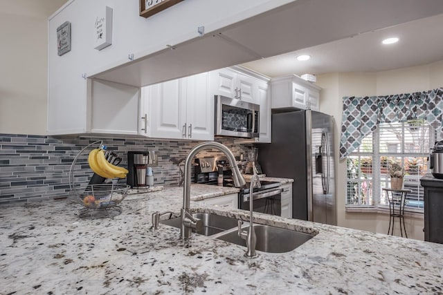 kitchen with white cabinets, appliances with stainless steel finishes, tasteful backsplash, sink, and light stone counters