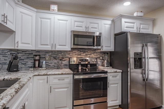 kitchen featuring decorative backsplash, white cabinets, a textured ceiling, and appliances with stainless steel finishes