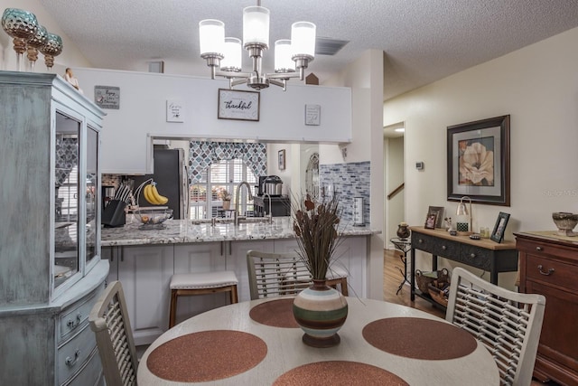 dining area featuring sink, a chandelier, and a textured ceiling