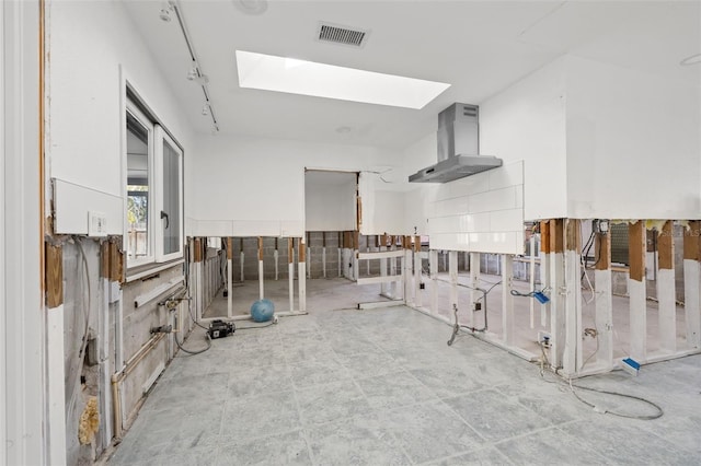 kitchen featuring rail lighting, wall chimney exhaust hood, and a skylight