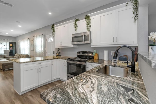 kitchen featuring white cabinets, appliances with stainless steel finishes, dark stone countertops, sink, and kitchen peninsula