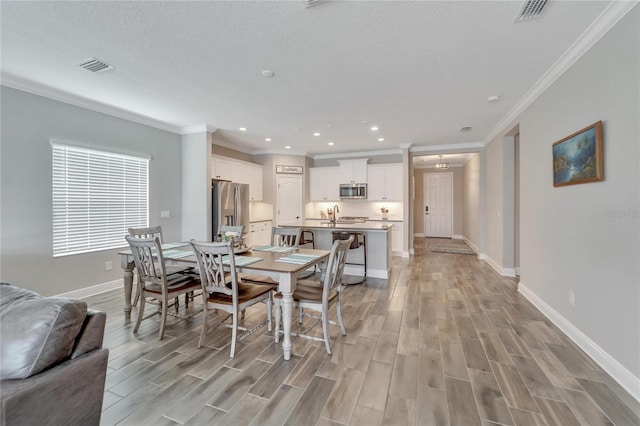 dining area featuring a textured ceiling, crown molding, and light wood-type flooring