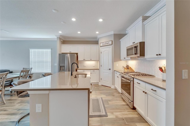 kitchen featuring white cabinets, stainless steel appliances, sink, a kitchen breakfast bar, and a kitchen island with sink