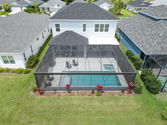 exterior space with glass enclosure, a patio area, a pool with hot tub, and a yard