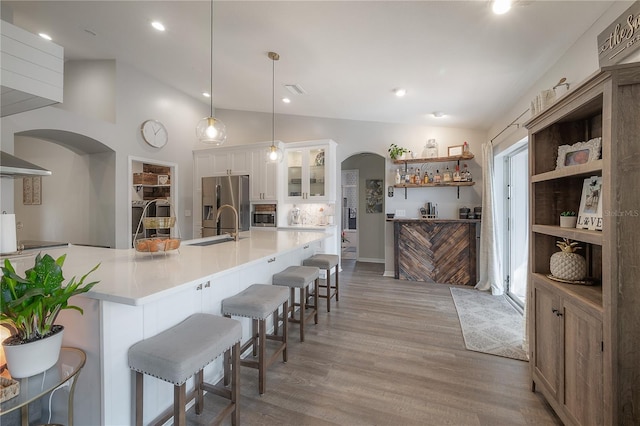 kitchen with stainless steel refrigerator with ice dispenser, vaulted ceiling, hanging light fixtures, white cabinetry, and a kitchen bar