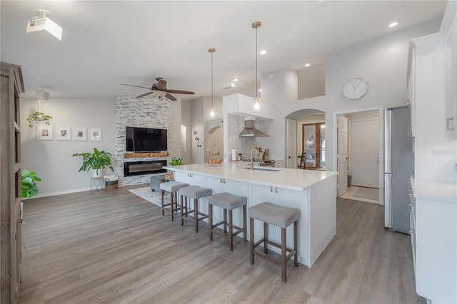 kitchen featuring pendant lighting, light wood-type flooring, white cabinetry, an island with sink, and a breakfast bar area