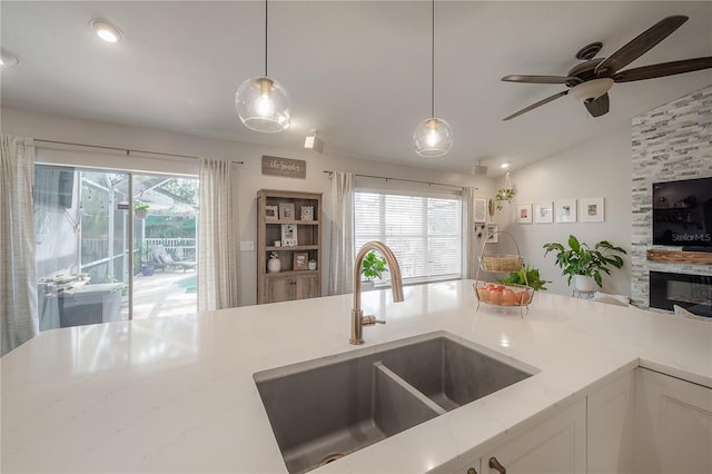 kitchen with light stone countertops, sink, white cabinets, pendant lighting, and lofted ceiling