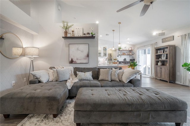 living room with light wood-type flooring, ceiling fan, lofted ceiling, and sink