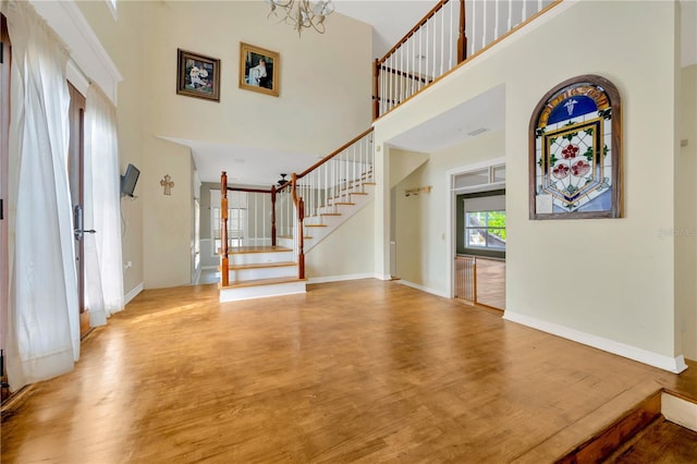 entryway featuring an inviting chandelier, a towering ceiling, and wood-type flooring