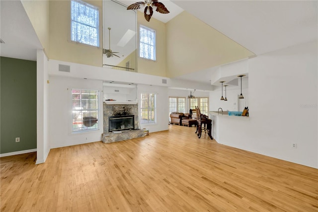 unfurnished living room featuring a towering ceiling, a fireplace, ceiling fan, and light hardwood / wood-style floors