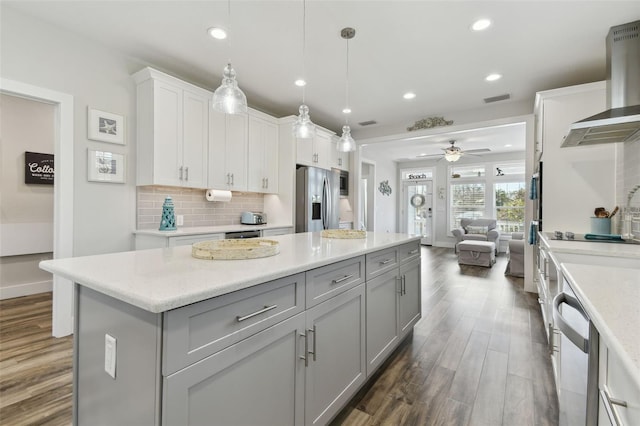 kitchen with pendant lighting, wall chimney range hood, dark wood-type flooring, appliances with stainless steel finishes, and backsplash