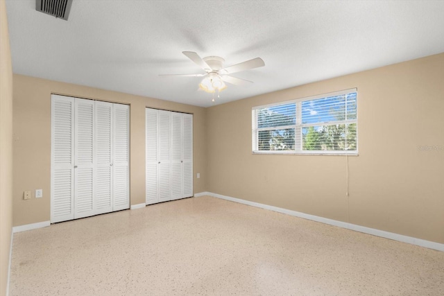 unfurnished bedroom with ceiling fan, a textured ceiling, and two closets