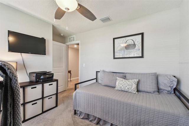 bedroom with a textured ceiling, a ceiling fan, visible vents, and light colored carpet