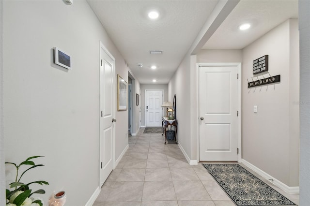 corridor with a textured ceiling, light tile patterned flooring, and baseboards