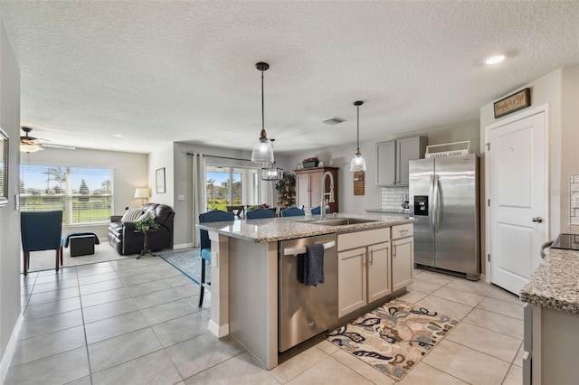 kitchen featuring light tile patterned floors, appliances with stainless steel finishes, open floor plan, a sink, and backsplash