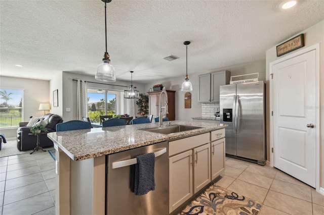 kitchen featuring a center island with sink, light tile patterned floors, appliances with stainless steel finishes, open floor plan, and a sink