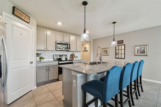 kitchen with a kitchen breakfast bar, a sink, gray cabinets, stainless steel appliances, and backsplash