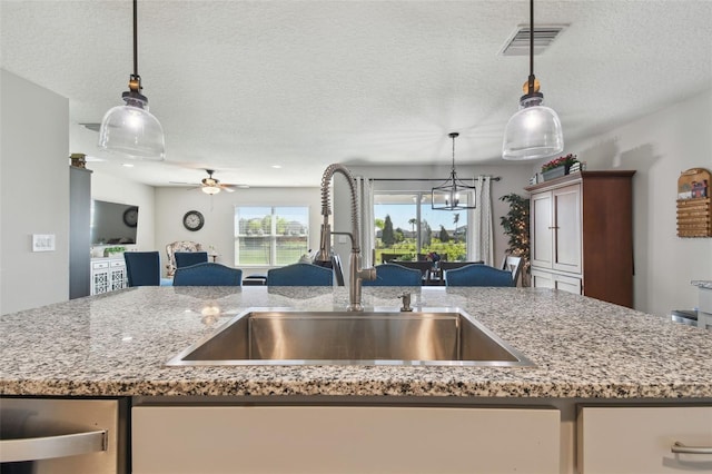 kitchen featuring visible vents, light stone counters, open floor plan, a kitchen island with sink, and a sink