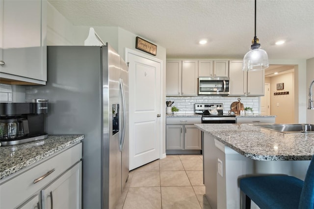 kitchen with decorative light fixtures, backsplash, appliances with stainless steel finishes, light tile patterned flooring, and a textured ceiling