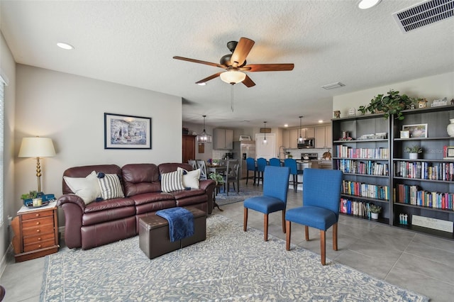 living area featuring light tile patterned floors, a textured ceiling, visible vents, and a ceiling fan