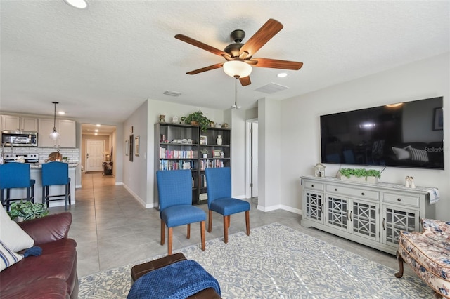 living area featuring light tile patterned floors, a textured ceiling, a ceiling fan, and baseboards