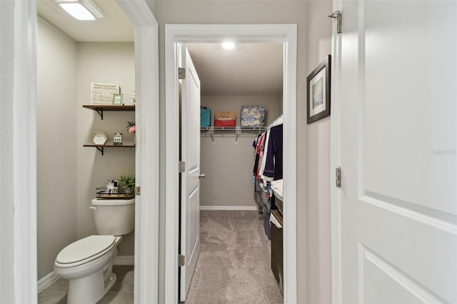 bathroom with a walk in closet, baseboards, a textured ceiling, and toilet