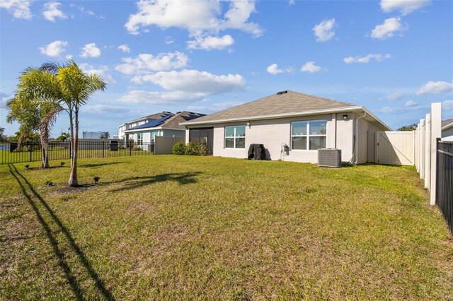 back of property with a fenced backyard, central AC, a lawn, and stucco siding