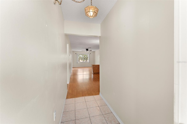 corridor with light tile patterned floors, baseboards, and a textured ceiling