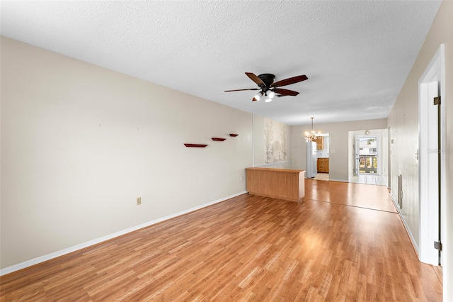 unfurnished living room featuring a textured ceiling, ceiling fan with notable chandelier, baseboards, and light wood-style floors