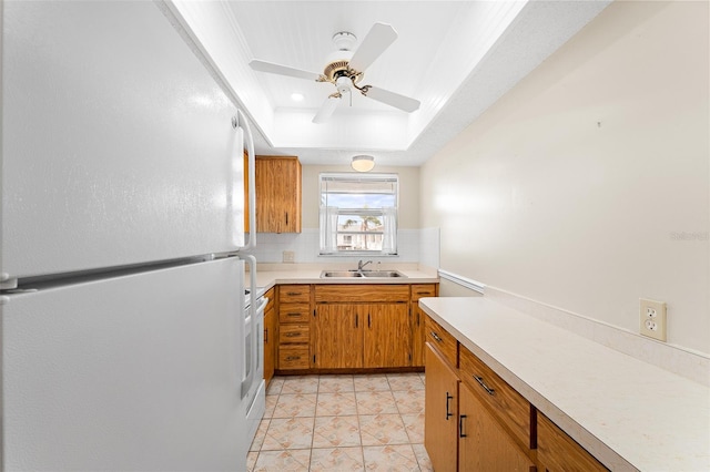 kitchen featuring a raised ceiling, freestanding refrigerator, a sink, light countertops, and backsplash