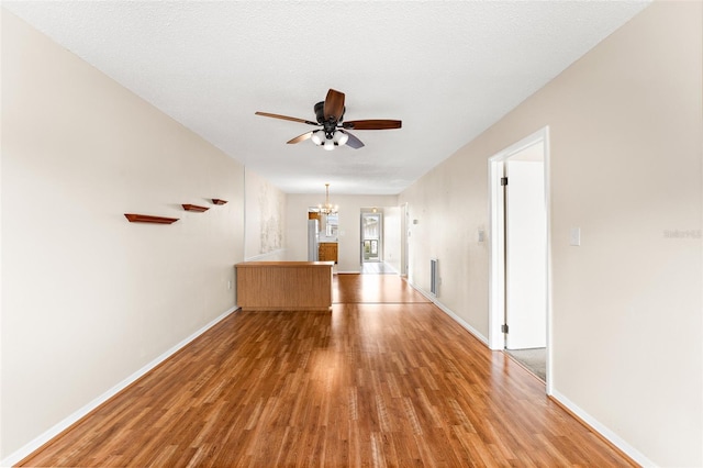 spare room featuring ceiling fan with notable chandelier, a textured ceiling, baseboards, and light wood-style floors