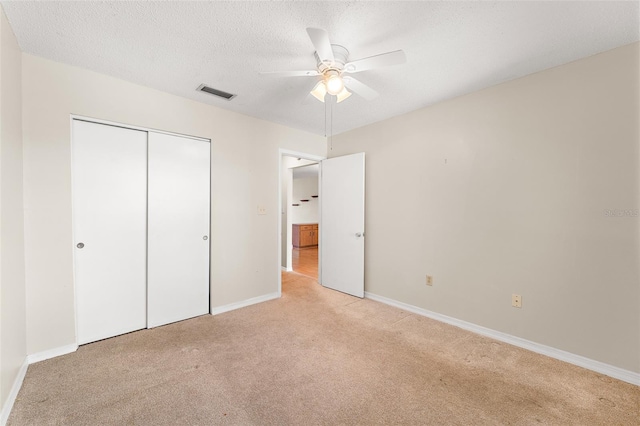 unfurnished bedroom featuring a textured ceiling, light colored carpet, visible vents, baseboards, and a closet