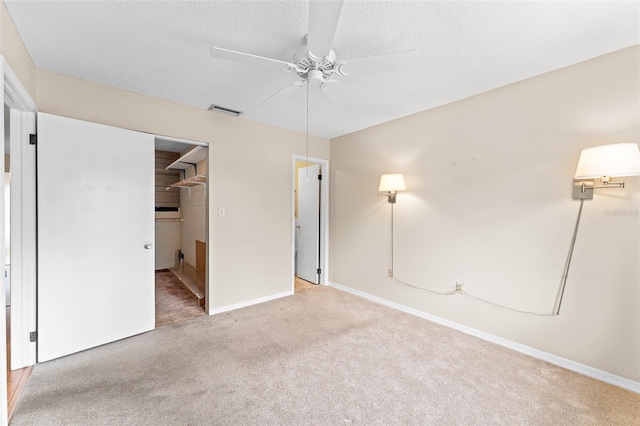 unfurnished bedroom featuring a walk in closet, visible vents, carpet flooring, a textured ceiling, and baseboards