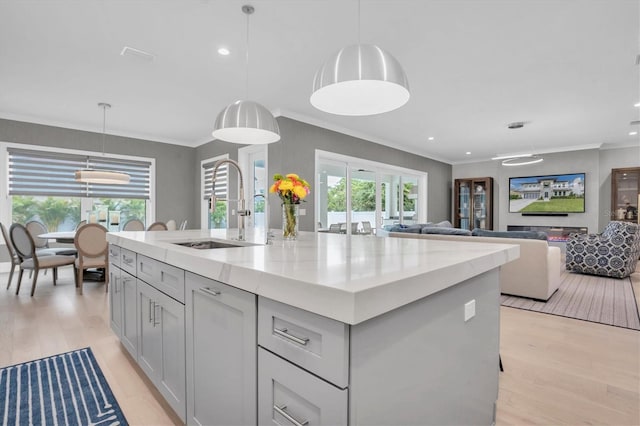 kitchen with sink, light stone counters, a center island with sink, light wood-type flooring, and pendant lighting