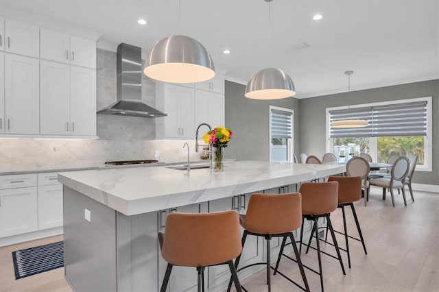 kitchen with pendant lighting, white cabinetry, an island with sink, and wall chimney range hood