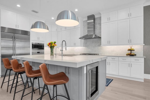 kitchen with wine cooler, white cabinets, appliances with stainless steel finishes, and wall chimney range hood