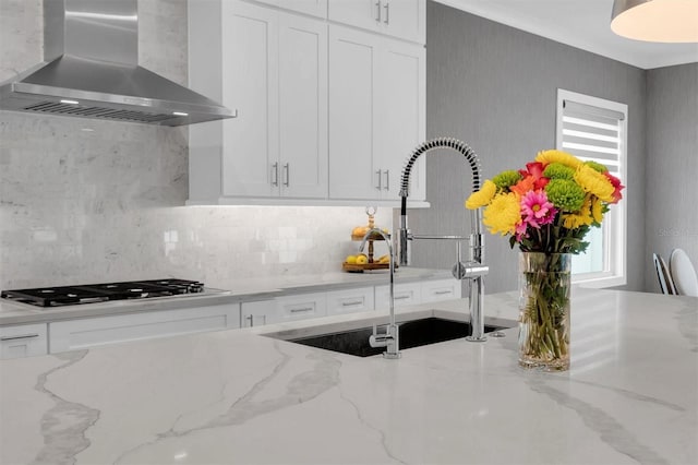 kitchen featuring white cabinetry, sink, stainless steel gas cooktop, light stone counters, and wall chimney exhaust hood