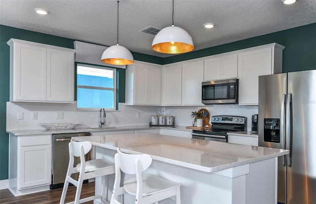 kitchen featuring a center island, light stone countertops, appliances with stainless steel finishes, white cabinetry, and decorative light fixtures