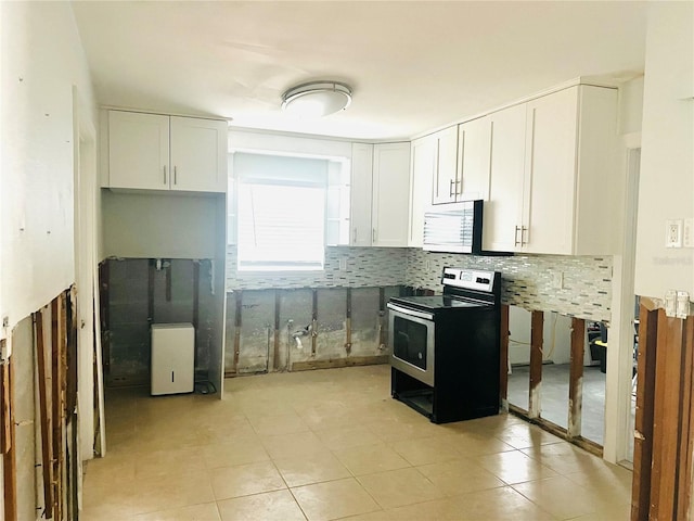 kitchen with white cabinetry, light tile patterned floors, decorative backsplash, a wood stove, and electric range