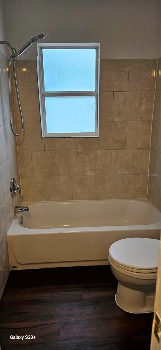 bathroom with hardwood / wood-style flooring, toilet, and tiled shower / bath