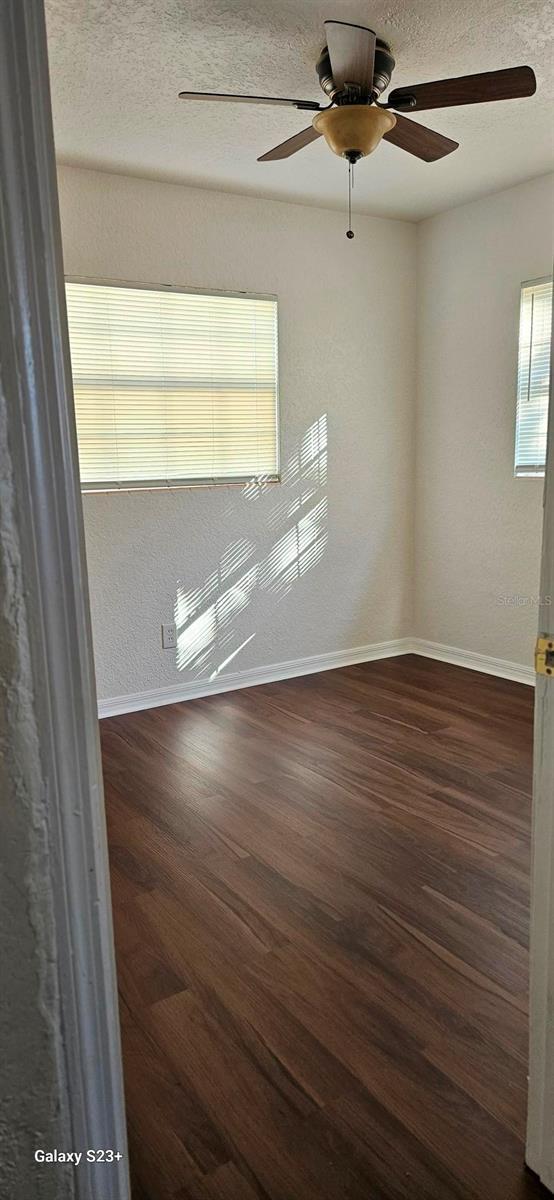 unfurnished room with ceiling fan, a textured ceiling, and dark hardwood / wood-style flooring