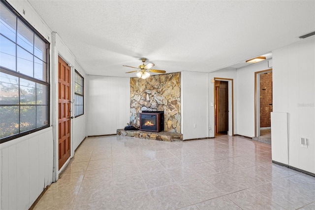 unfurnished living room with ceiling fan, a stone fireplace, and a textured ceiling