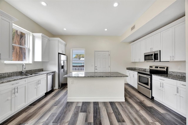 kitchen featuring stainless steel appliances, white cabinetry, a kitchen island, and dark stone countertops