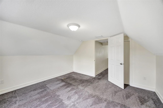 additional living space featuring lofted ceiling, a textured ceiling, and dark carpet