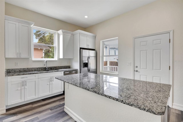 kitchen featuring sink, dark stone countertops, stainless steel appliances, white cabinets, and a kitchen island