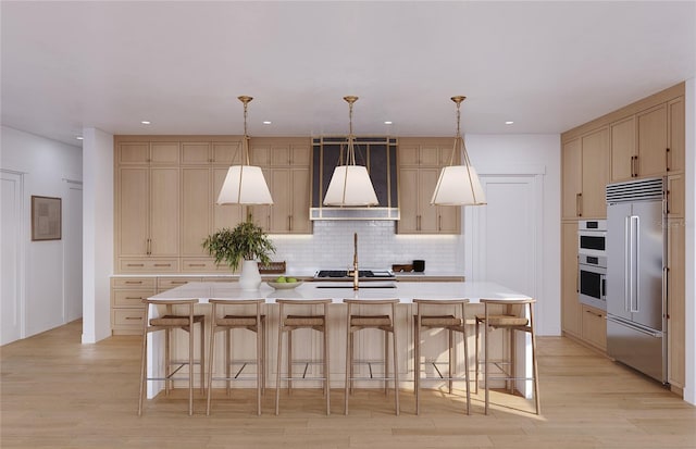 kitchen featuring built in refrigerator, pendant lighting, a center island with sink, and light hardwood / wood-style flooring