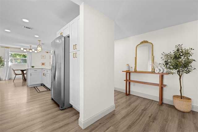 hallway with an inviting chandelier and light hardwood / wood-style flooring