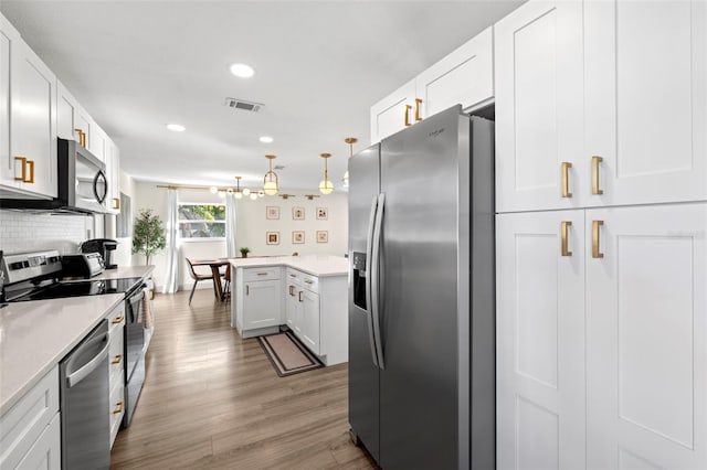 kitchen featuring decorative light fixtures, white cabinets, backsplash, stainless steel appliances, and light wood-type flooring